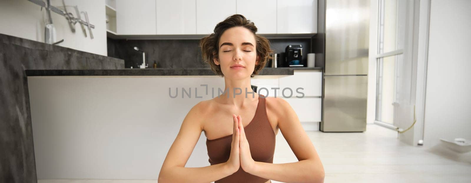 Portrait of female athlete, girl practice yoga, meditating in lotus pose, using mindfulness technique, workout at home on kitchen floor by Benzoix