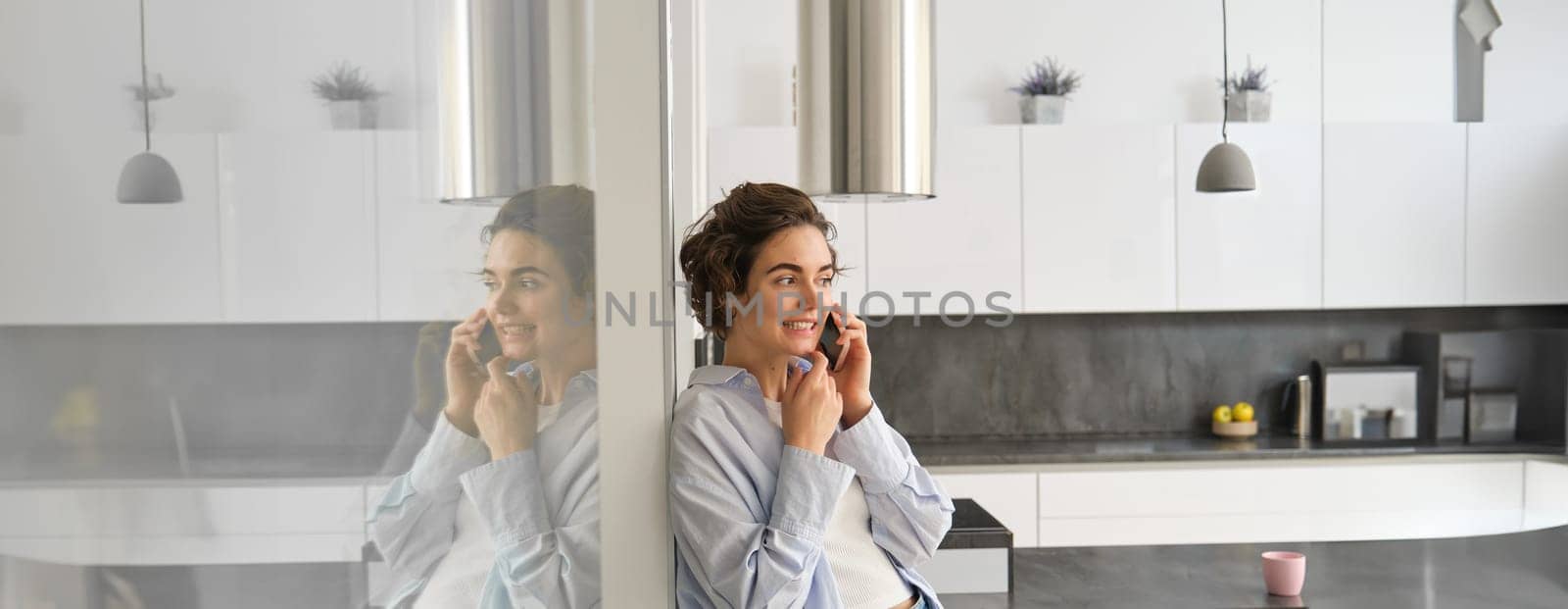 Portrait of cute young woman answers a phone call, talks on smartphone, spends time at home by Benzoix