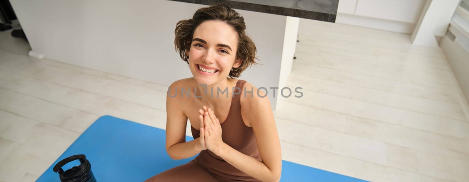 Peace, mindfulness and meditation. Young smiling sportswoman, fitness girl sits at home on floor and meditating, doing yoga, relaxing in lotus pose.