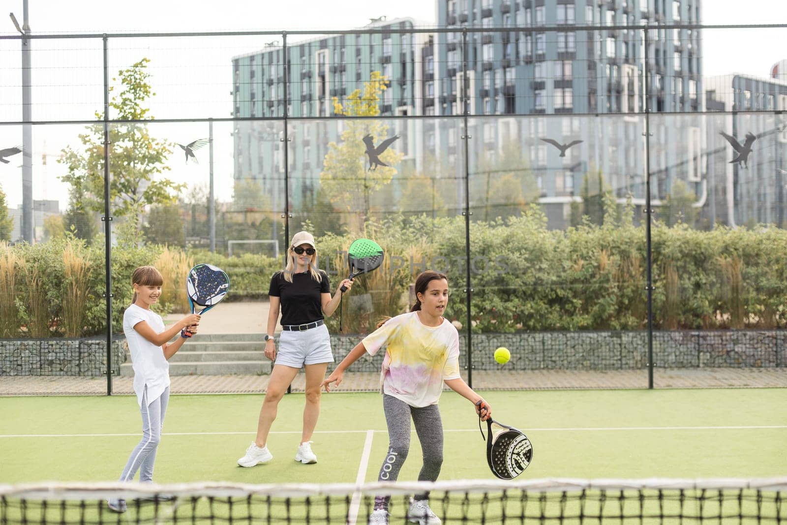 Cheerful coach teaching child to play tennis while both standing on tennis court. High quality photo
