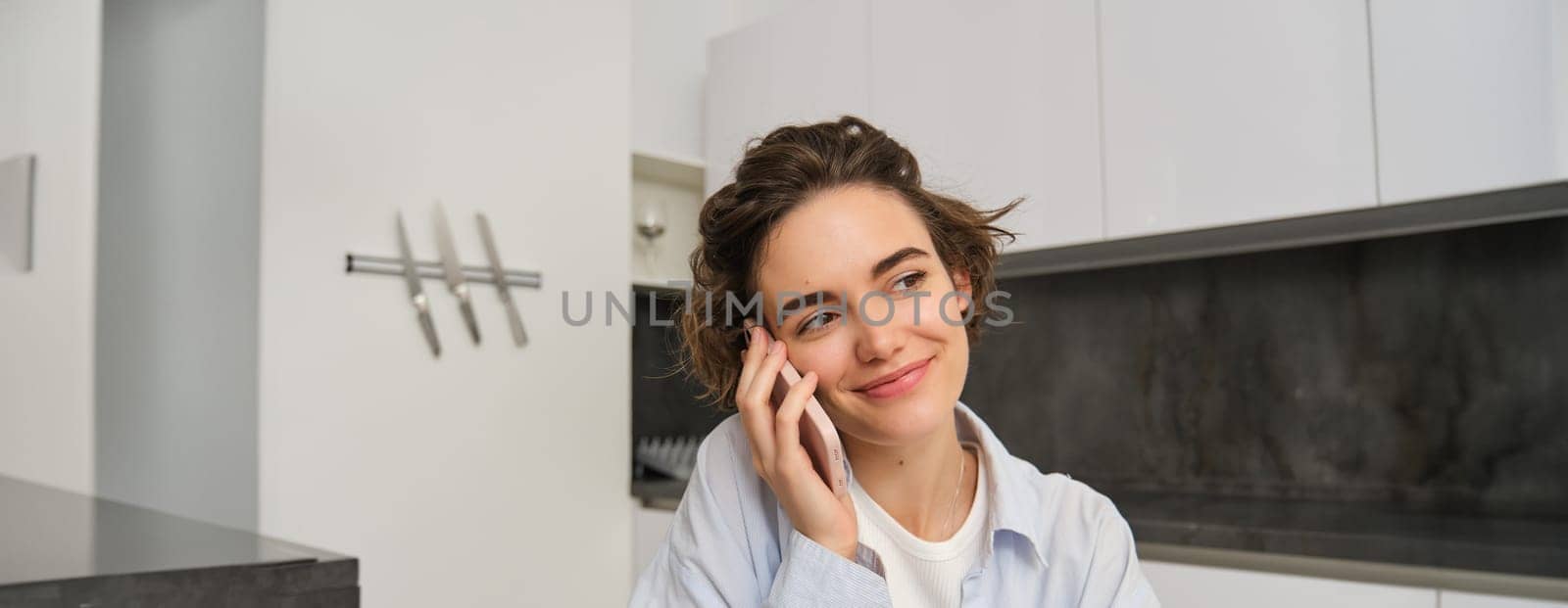 Image of woman working at home, making a phone call, sitting with smartphone, surrounded with paperwork, doing homework and talking to someone by Benzoix