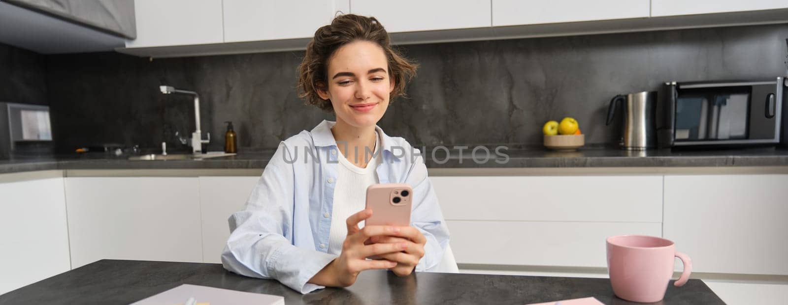 Portrait of beautiful smiling woman sitting at home with smartphone, using mobile phone app, orders groceries delivery by Benzoix