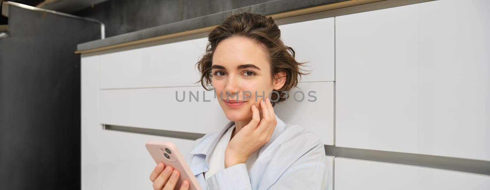 Portrait of girl with mobile phone, sits on floor at home, orders takeaway in app. Young woman with smartphone does online shopping from home, browsing websites.