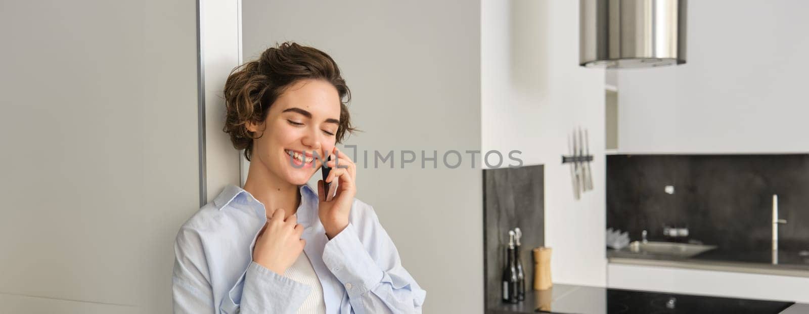 Portrait of woman talking on mobile phone and smiling, spending time at home, has telephone conversation, answers a call by Benzoix