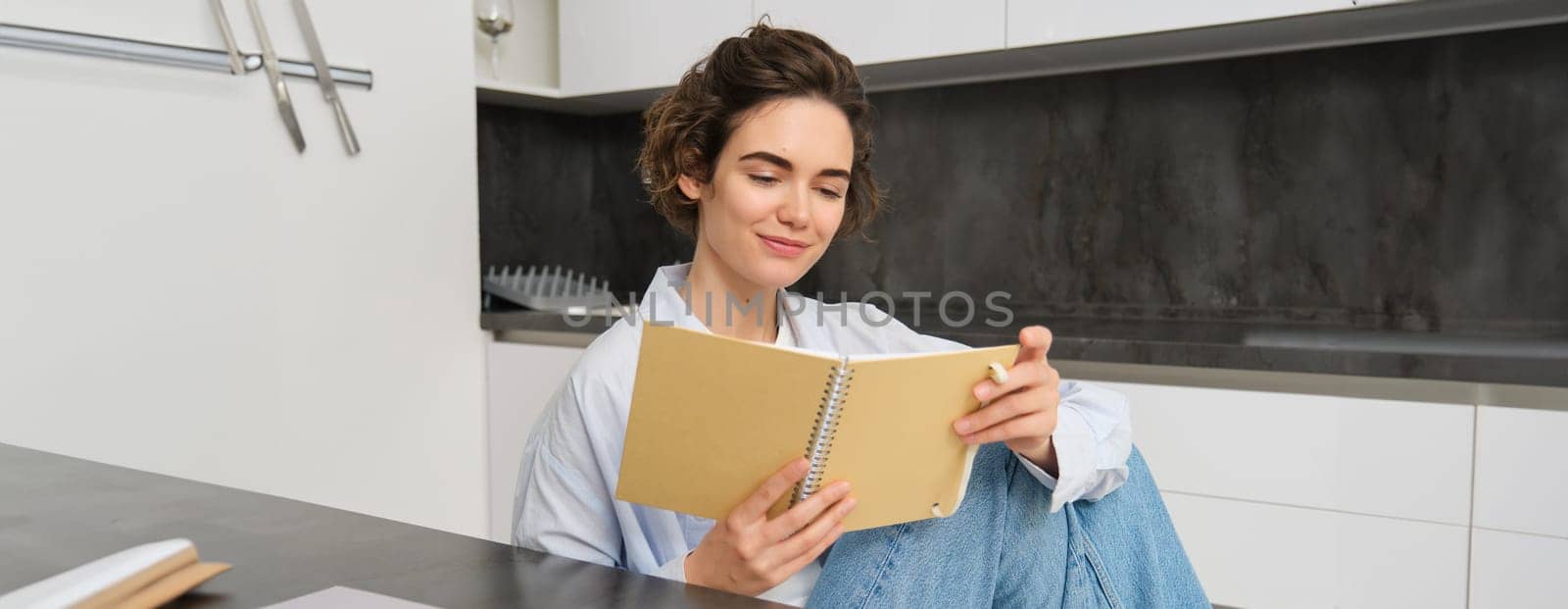 Image of brunette girl reading through her notes, writing in journal, studying while sitting at home.