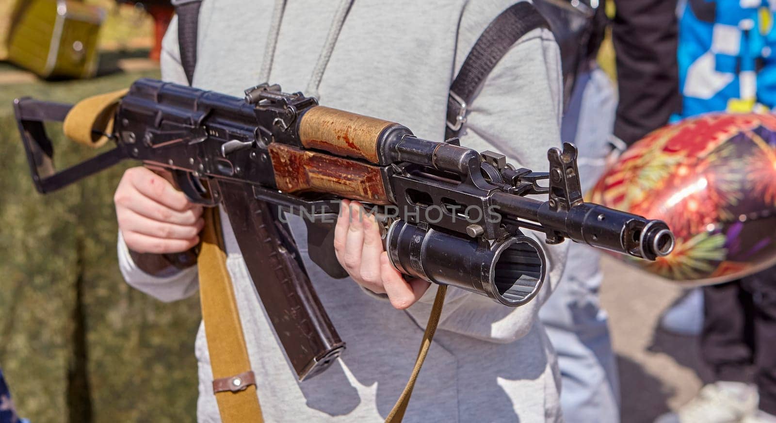 Close-up of a girl with a Kalashnikov assault rifle. Children's hands hold weapons.