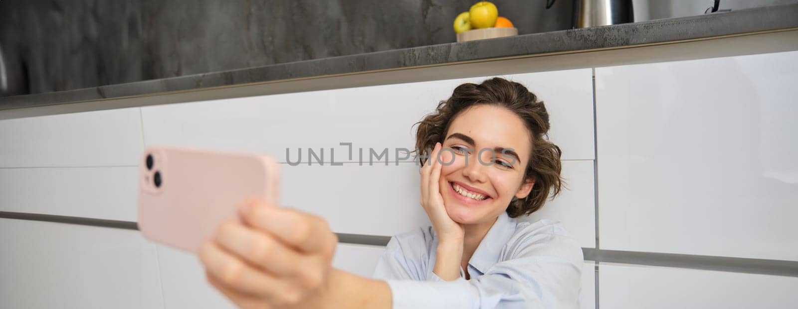 Portrait of happy, beautiful woman takes selfie on smartphone, extends her hand with mobile phone and takes picture of herself, records vlog on mobile phone.