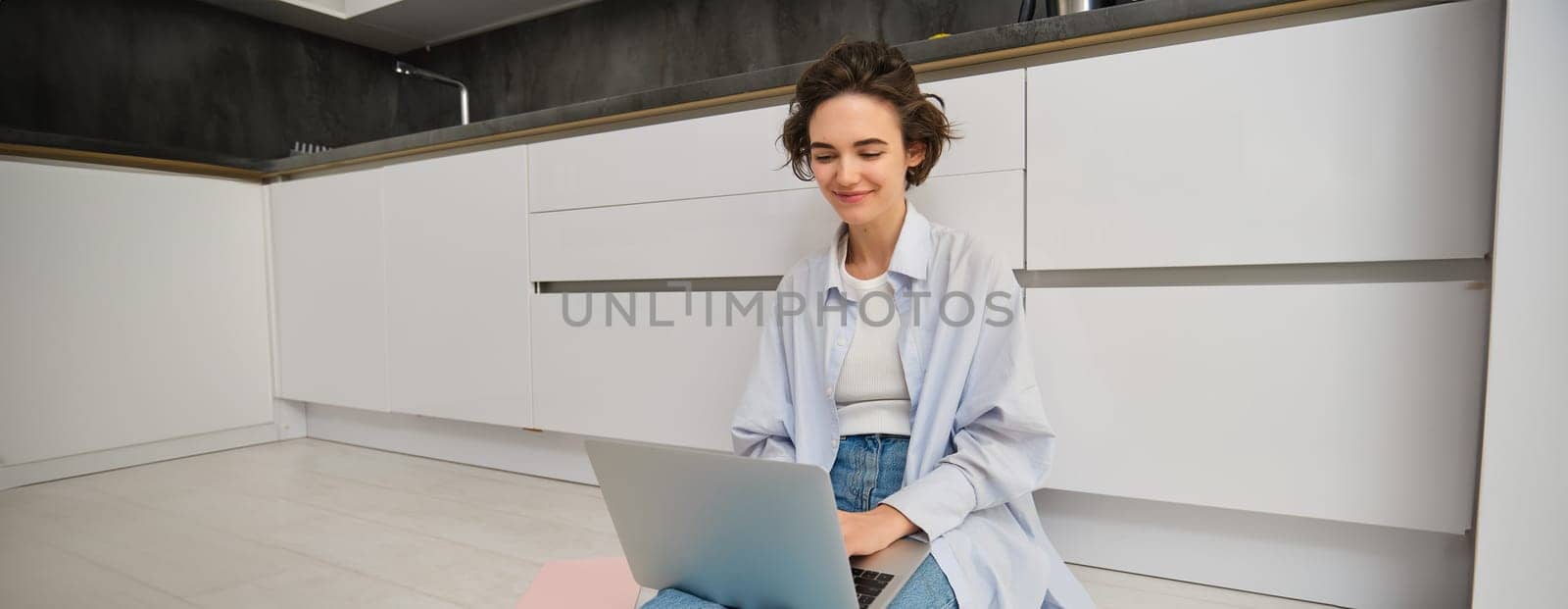 Young IT girl, woman works freelance from home, sits on floor with laptop. Girl student does homework online, writes on computer keyboard by Benzoix