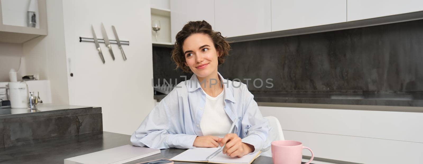 Portrait of young woman at home, working, writing in notebook, taking notes or doing homework.