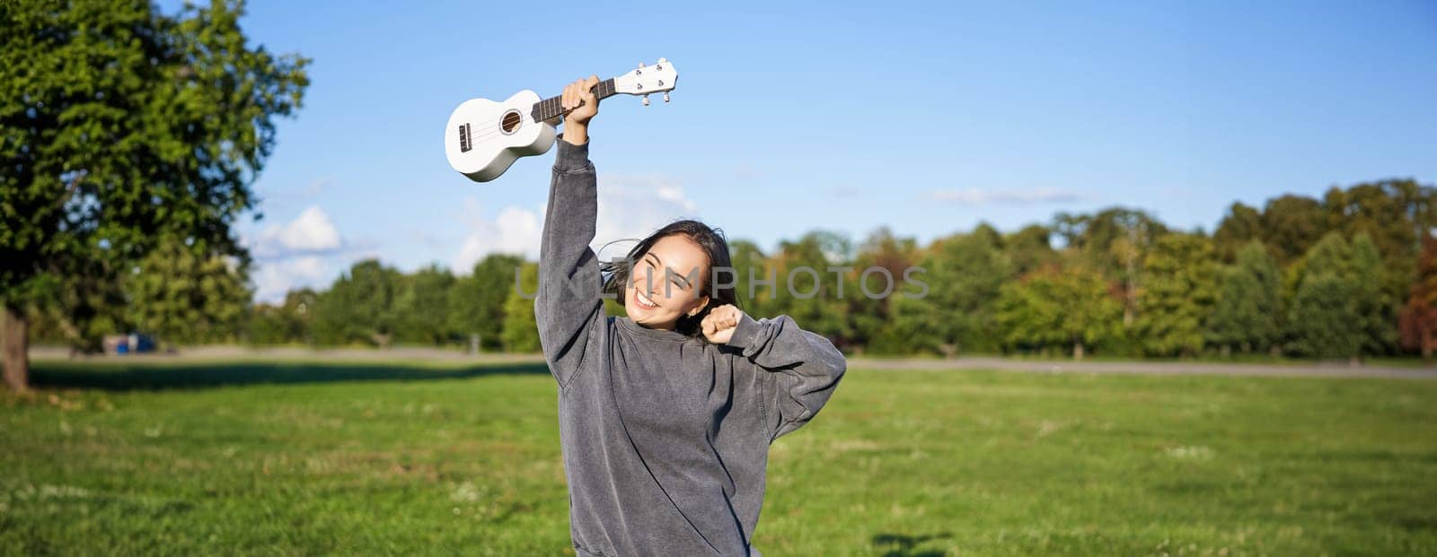 Positive beauty girl with ukulele, dancing and feeling freedom, looking excited, triumphing and celebrating.