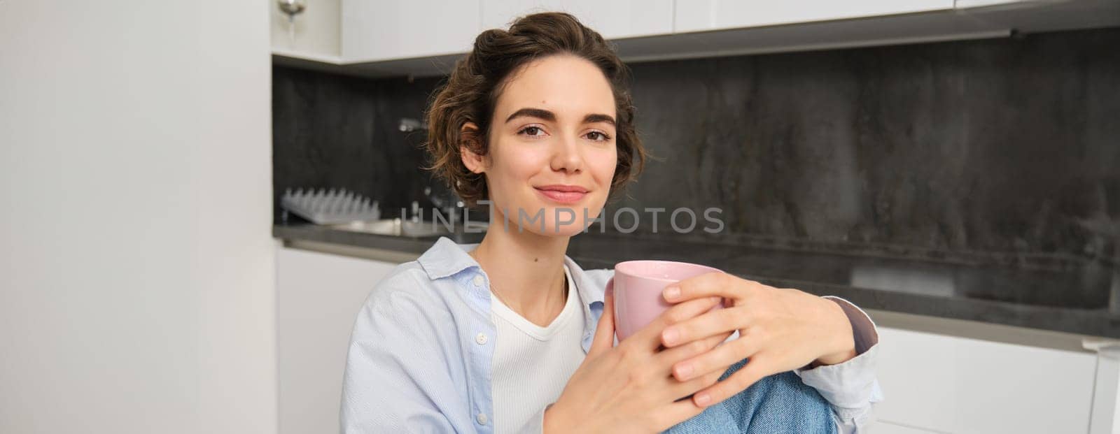 Portrait of smiling woman with cup of tea, drinking hot beverage at home, looking relaxed, enjoying comforting weekend.