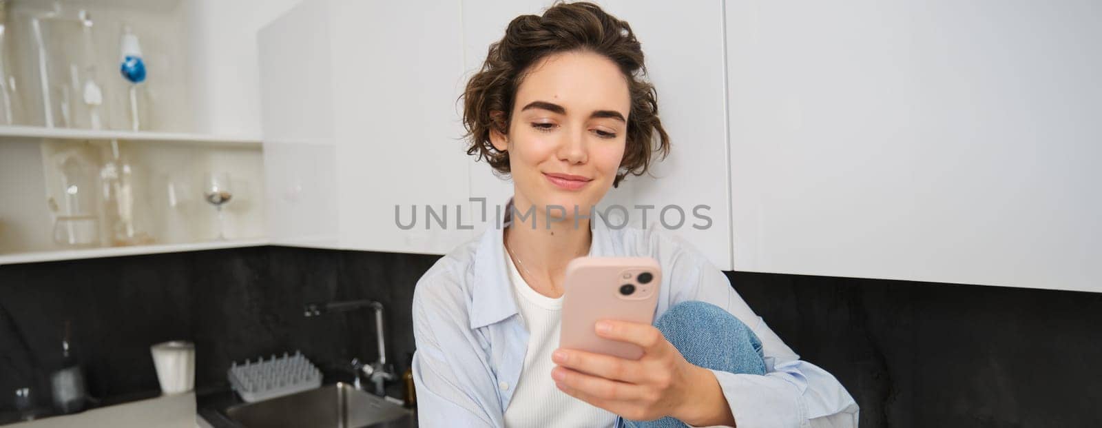 Portrait of young woman checking her mobile phone, reading message on smartphone and smiling.