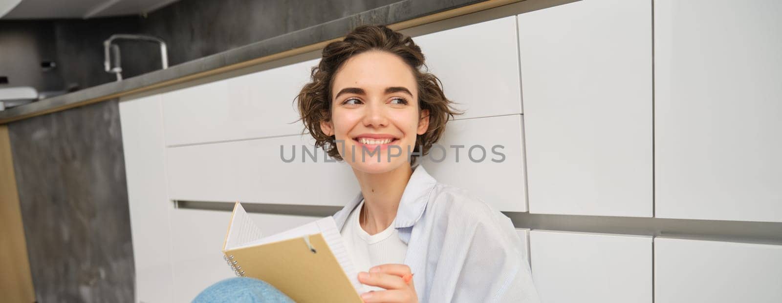 Close up portrait of young woman writing in her journal, feeling creative, sitting with planner, notebook and pen on floor, studying, doing her homework at home.