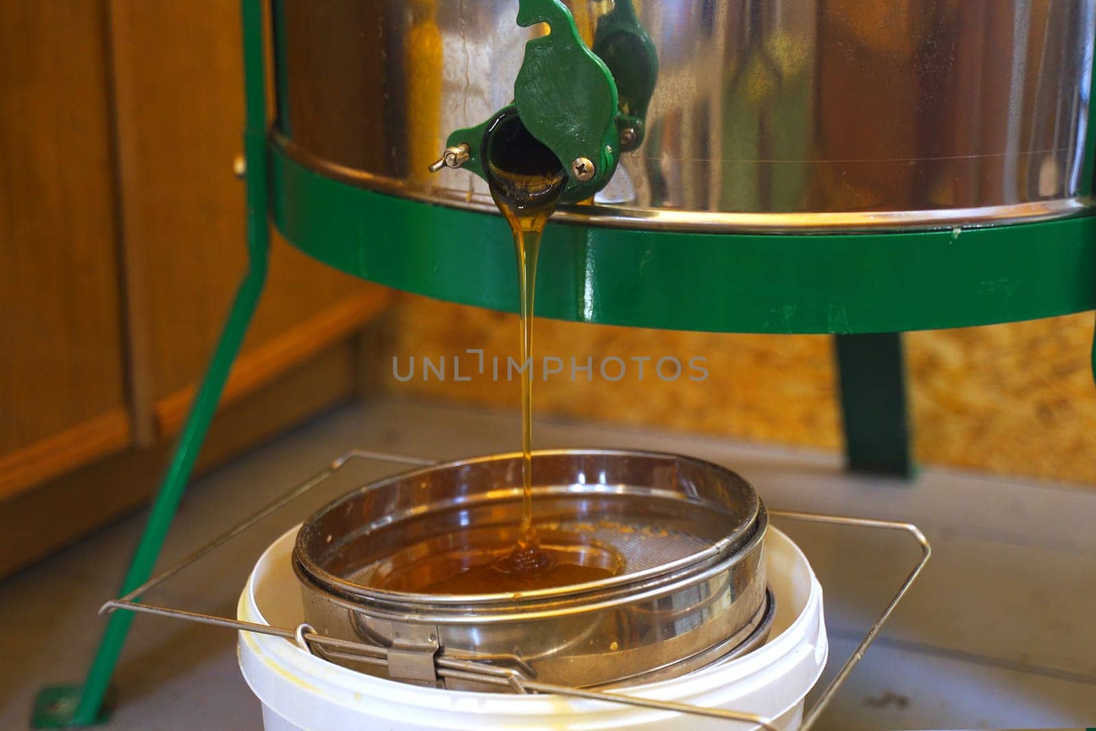 Honey production. The beekeeper opens the honey extractor valve and the honey flows out of the extractor onto the filter sieve.