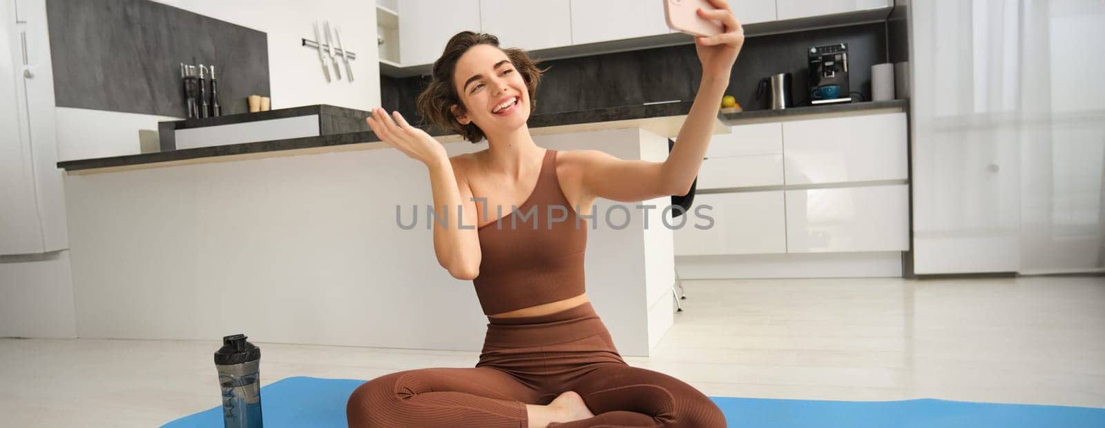 Sporty young female athlete, girl takes selfie on smartphone, workout from home and makes pictures, records video on phone during fitness exercises by Benzoix