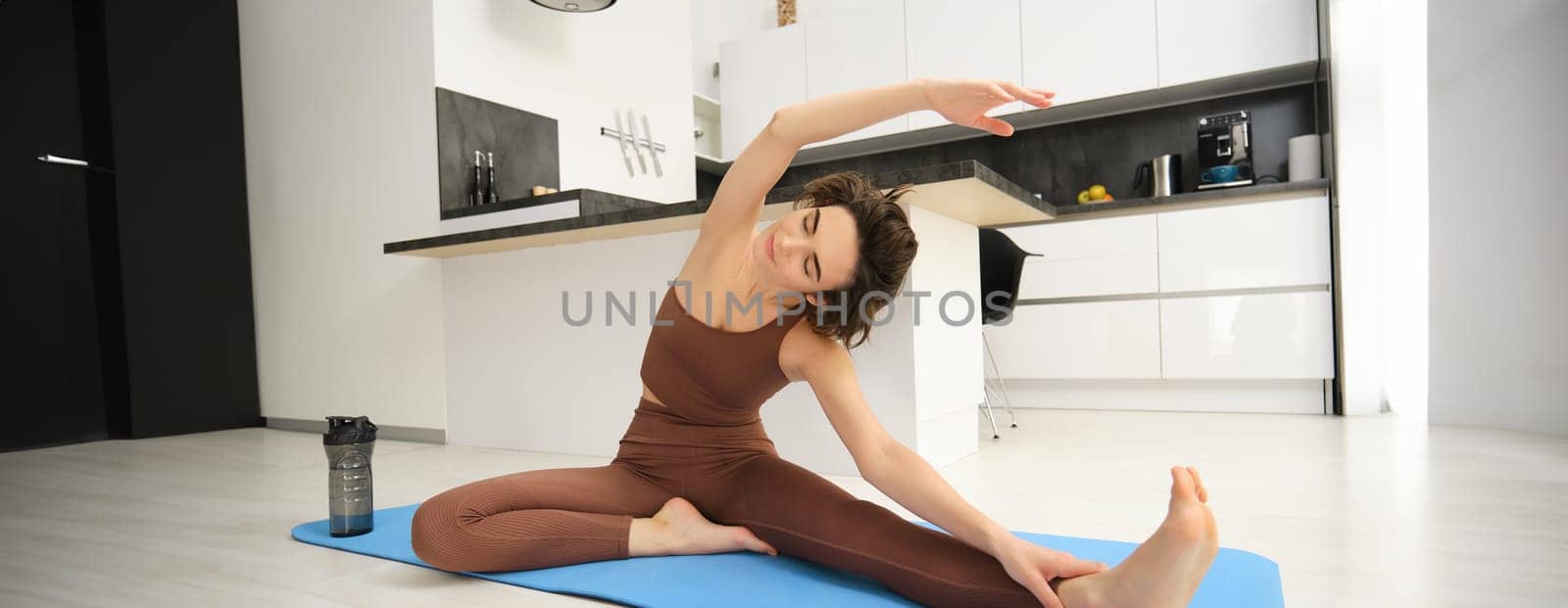 Image of brunette girl, stretching her legs, doing fitness workout, feet exercises to warm up before yoga, training at home alone.
