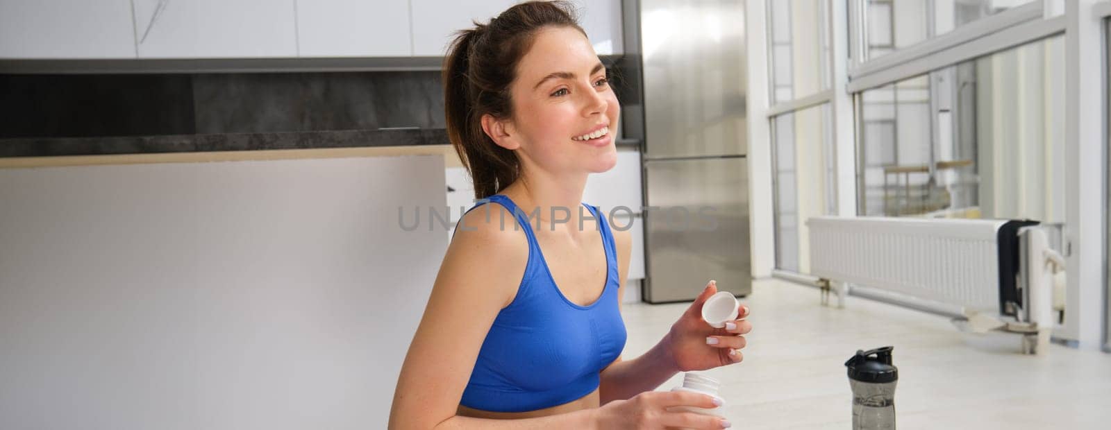 Portrait of beautiful and healthy fitness woman, taking vitamins, dietary supplements for muscles and bones, doing workout training at home by Benzoix