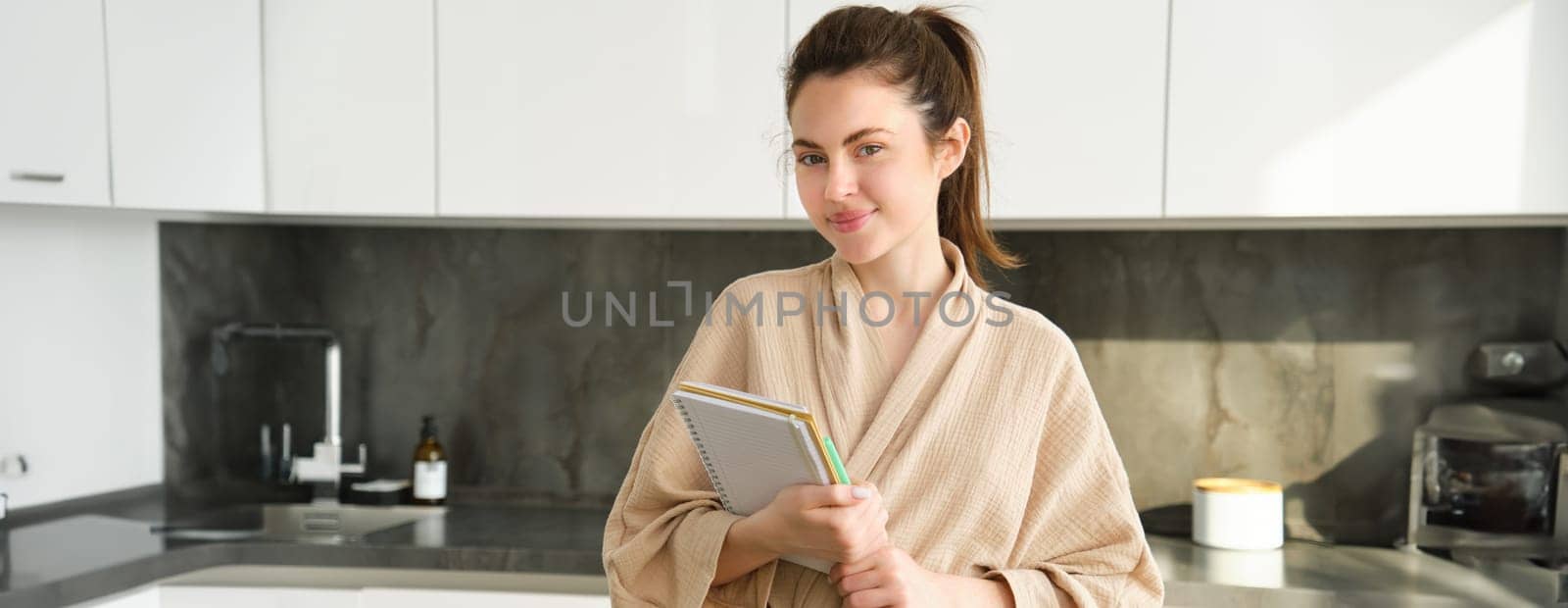 Portrait of woman preparing grocery list, writing down food ideas, creating new recipe in the kitchen, thinking of meal list for dinner, standing in bathrobe by Benzoix