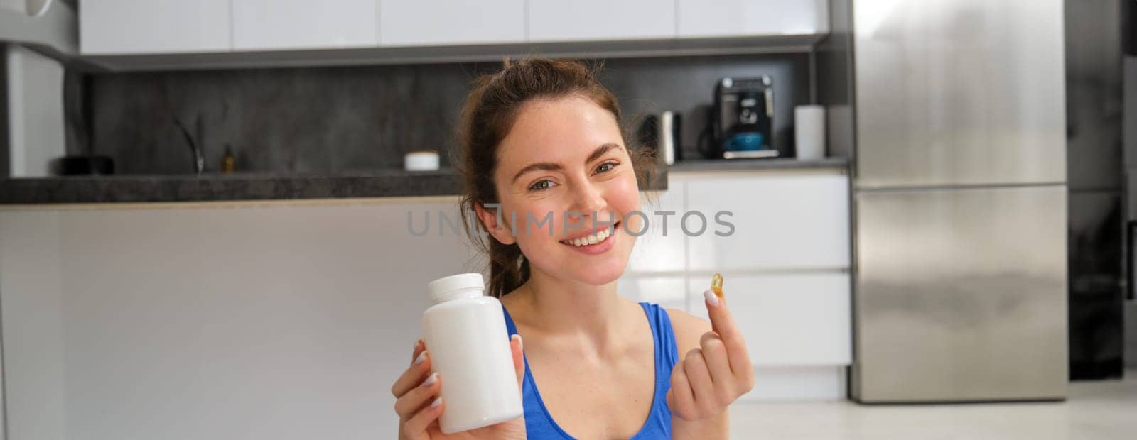 Happy young fit girl, doing sports at home, shows dietary supplements, taking vitamins for healthy body, recommending, showing drug capsule.