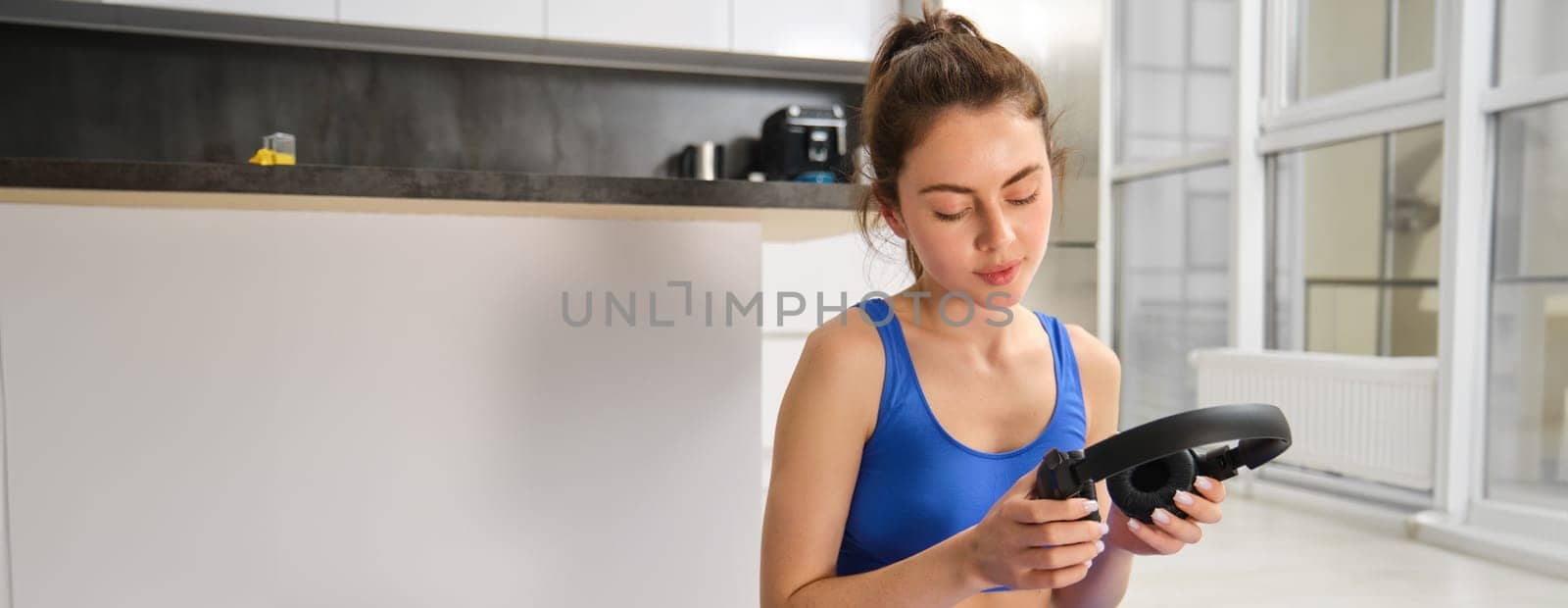 Portrait of woman doing home fitness exercises on yoga mat, listening music in wireless headphones, focusing on workout in earphones by Benzoix