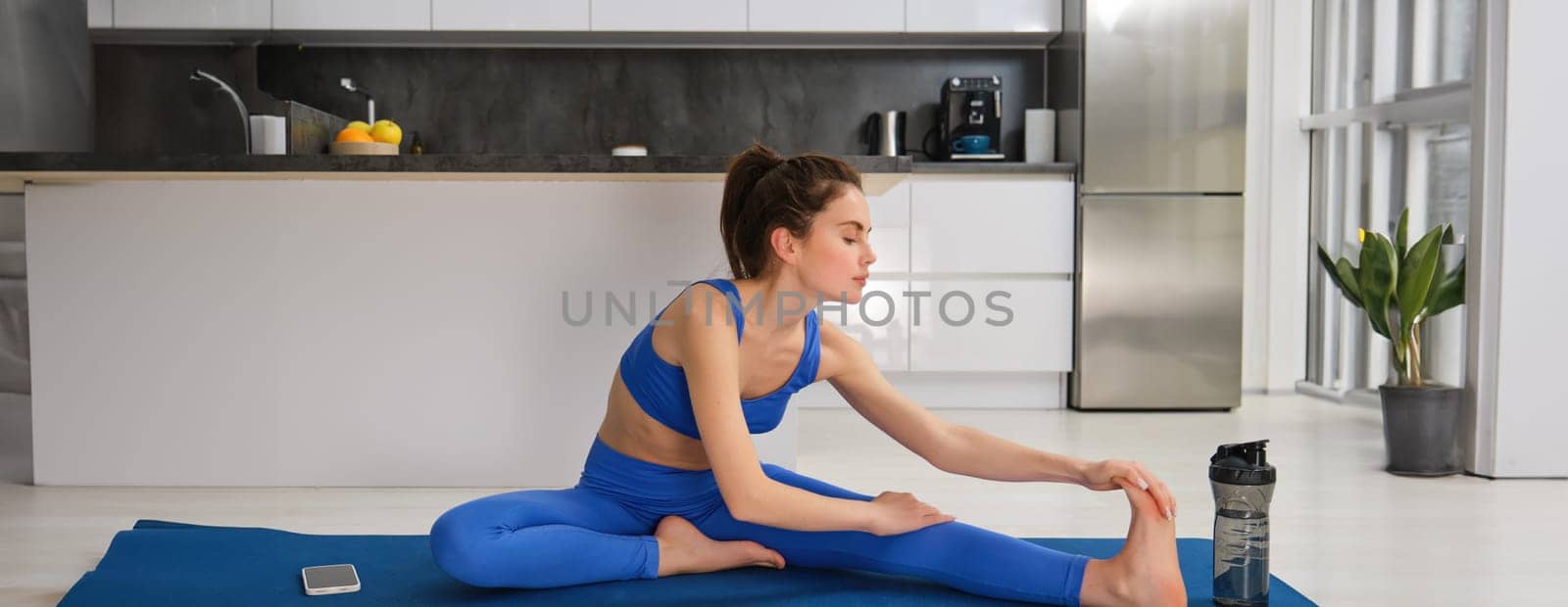 Fitness and workout concept. Young woman stretching her legs, doing exercises at home on yoga mat, doing splits on floor in living room.