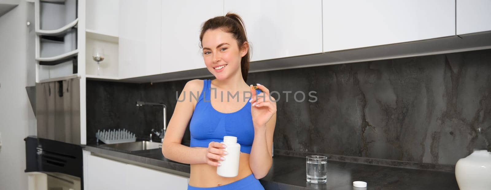 Sport and healthcare. Young woman holding tablets, vitamin c, taking dietary supplements and smiling, leading active and healthy lifestyle, wearing sportswear.