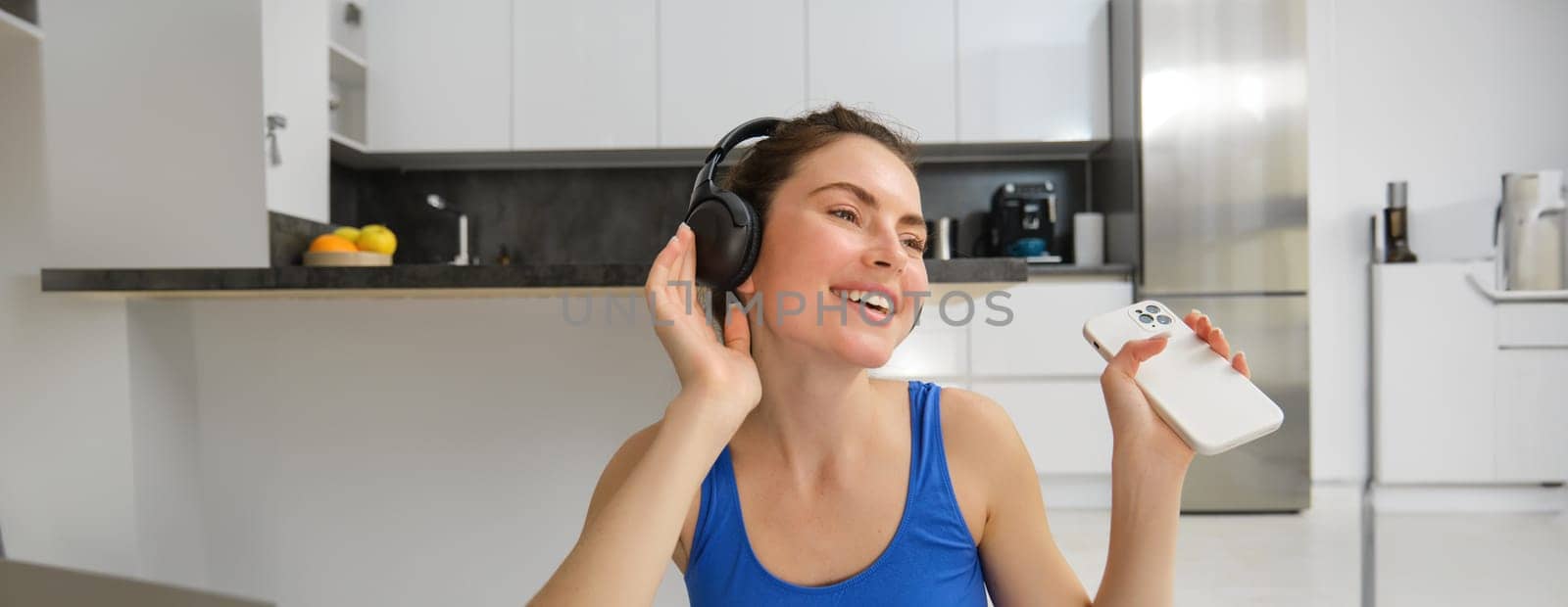 Happiness, sports and wellbeing. Young woman dancing in headphones, holding smartphone, doing workout at home, fitness training inside her house.