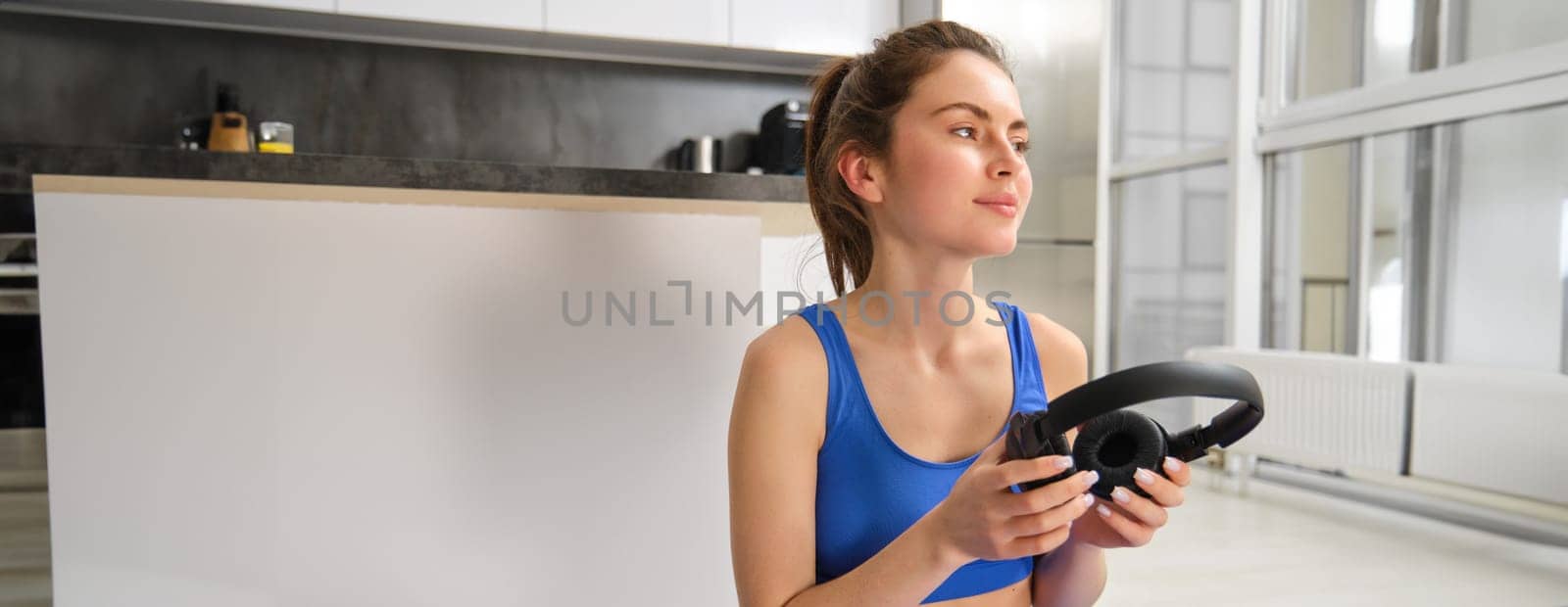Young woman, fitness instructor doing workout at home, practice yoga in wireless headphones on rubber mat.