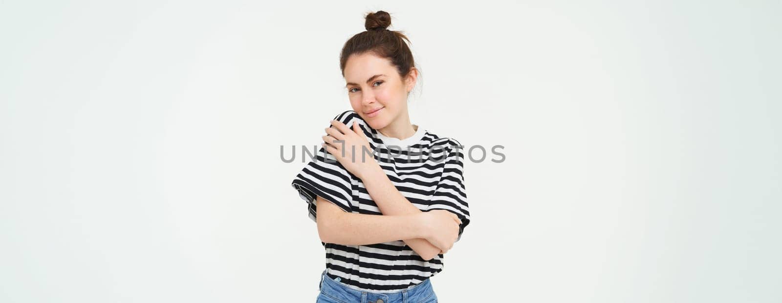 Image of tender, beautiful brunette girl, hugging herself, concept of selfcare and love, standing over white background.