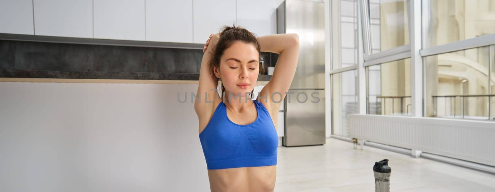Fitness, yoga and gym at home concept. Young woman doing stretching workout, exercising in living room, fitness training indoors by Benzoix