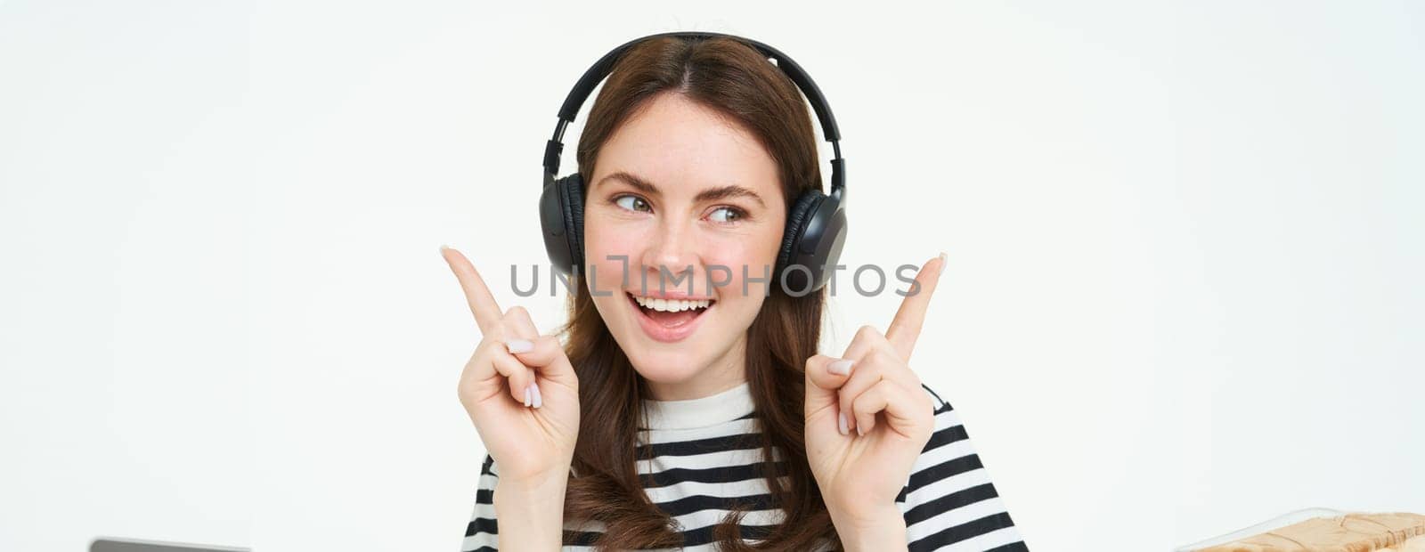 Dancing girl in wireless headphones pointing at empty space for music store promo text, showing advertisement, isolated over white background by Benzoix