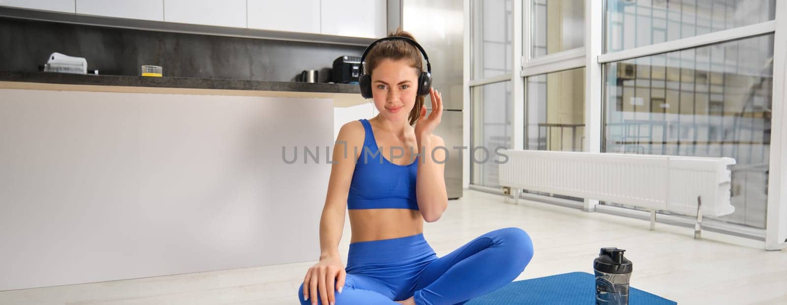 Portrait of woman doing home fitness exercises on yoga mat, listening music in wireless headphones, focusing on workout in earphones.