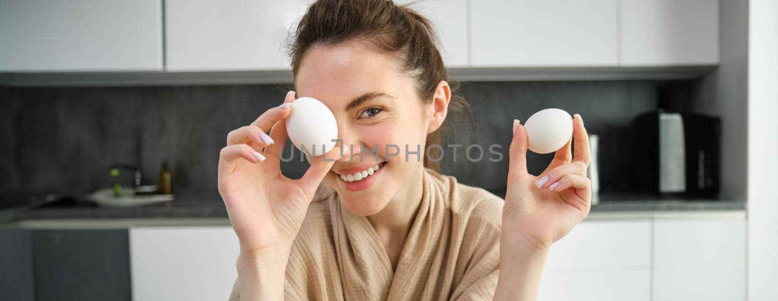 Attractive young cheerful girl baking at the kitchen, making dough, holding recipe book, having ideas.