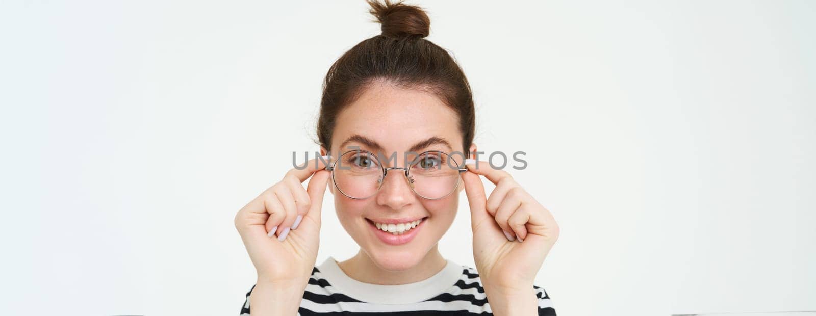 Close up portrait of beautiful woman, trying on new glasses, buying eyewear, smiling and looking happy, standing over white background.