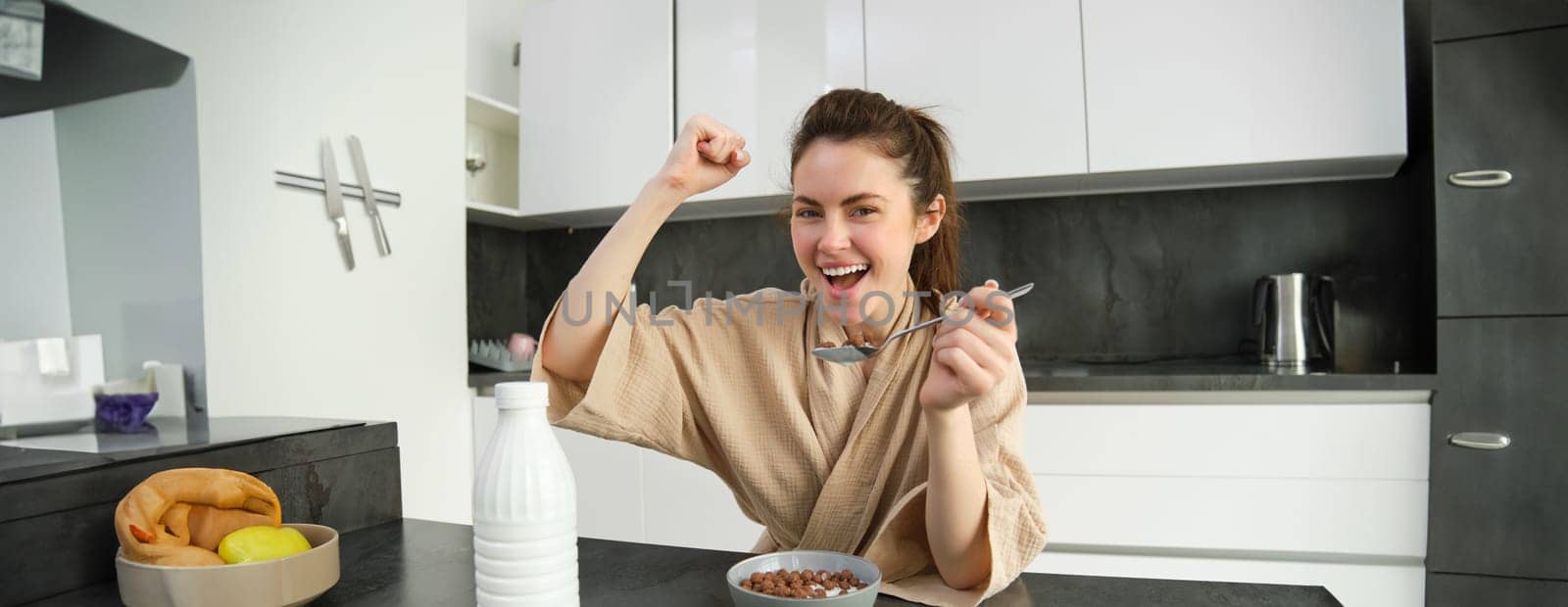 Portrait of happy, laughing young woman eating cereals with milk, triumphing, having breakfast and feeling excited, energetic morning concept.