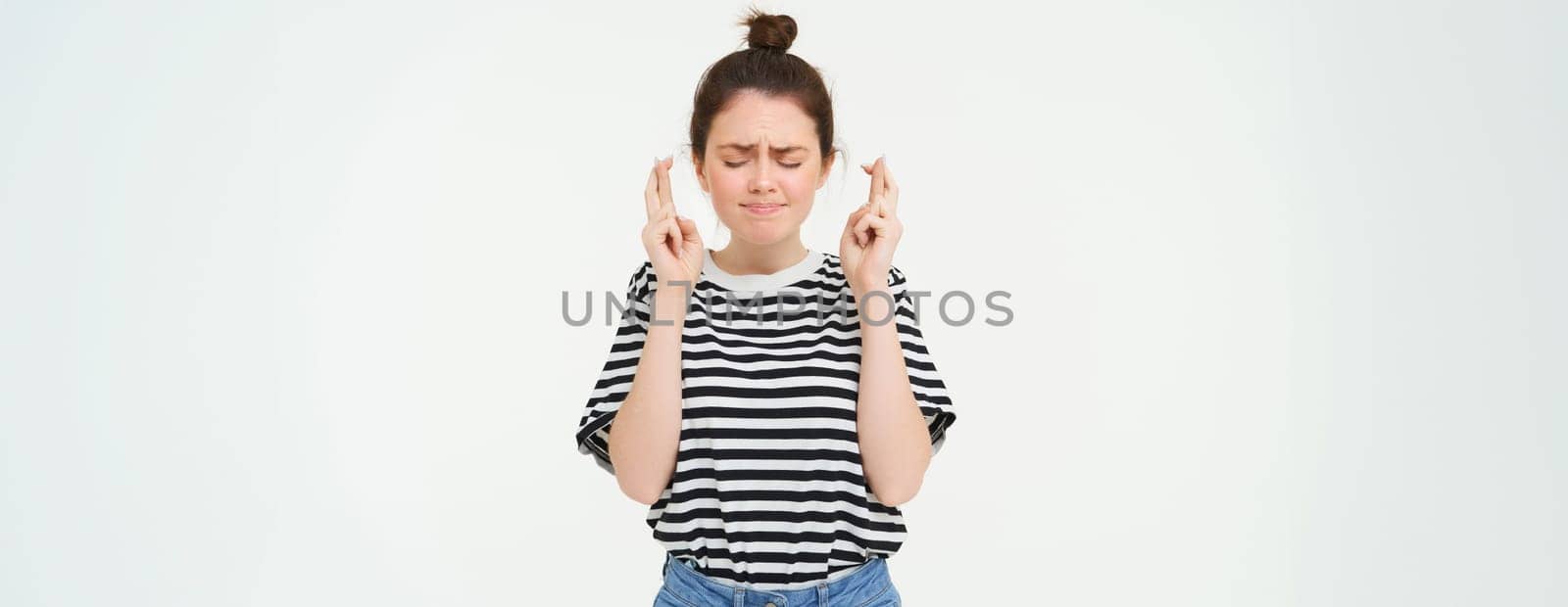 Nervous girl, student cross fingers for good luck, making wish, hoping for something, anticipating positive results, standing over white background.