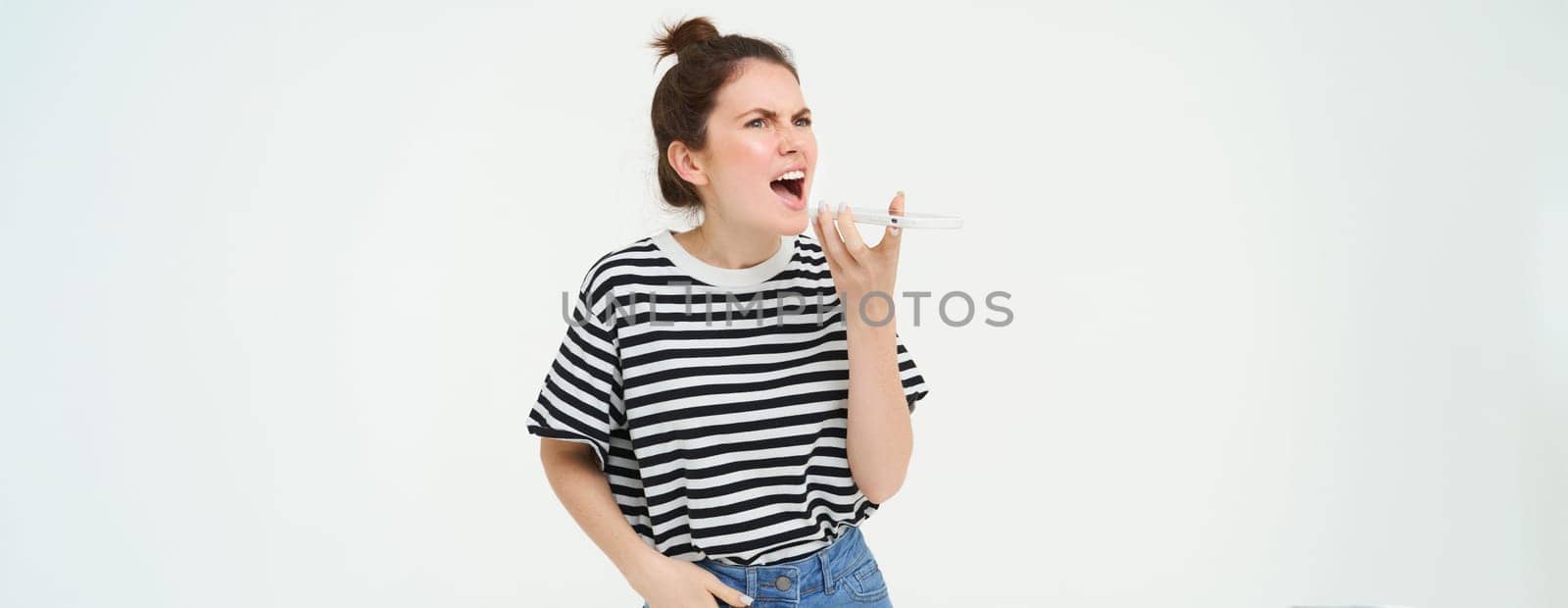 Angry woman shouts at mobile phone, argues at someone over the telephone, has intense conversation over smartphone, white background.
