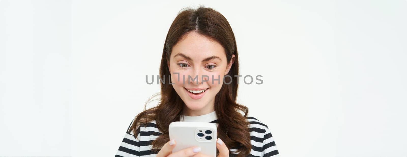 Portrait of woman looking surprised at mobile phone screen, reads amazing promo in online store, standing over white background.