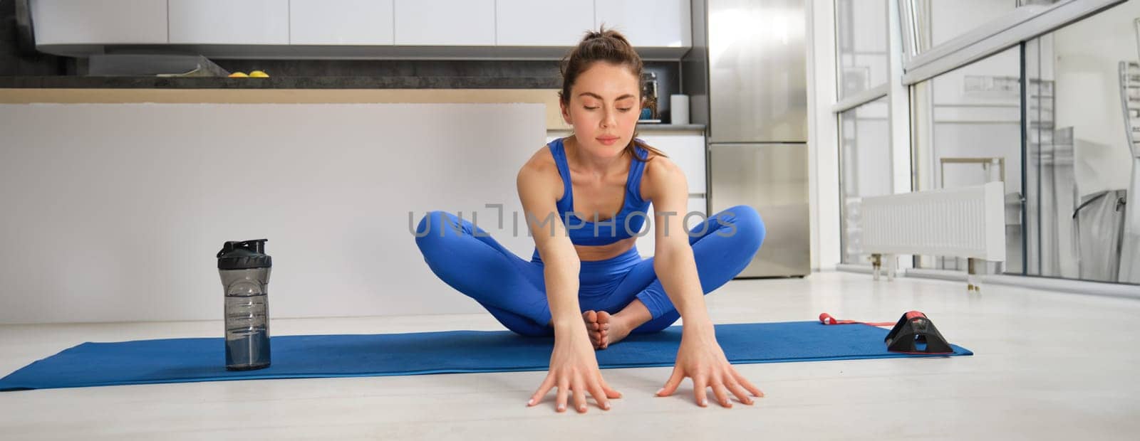 Young woman does sport exercises, fitness workout in living room, workout from home on rubber blue mat.