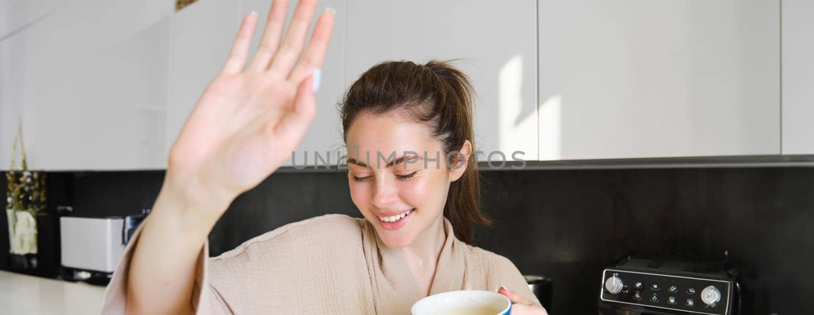 Portrait of beautiful girlfriend covers her face from camera and giggles, holding cup of coffee, concept of romantic mornings at home.