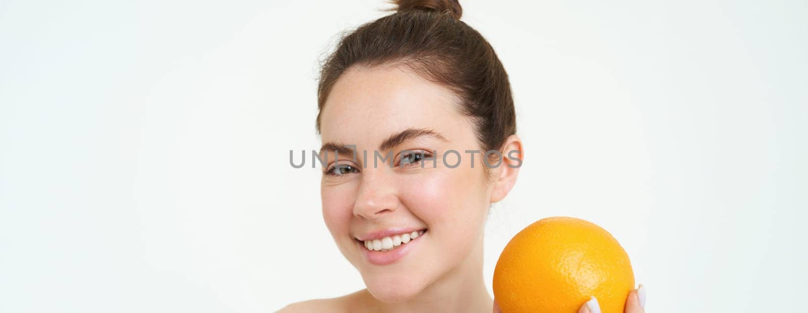 Vitamin C and health concept. Young beauty woman, holding orange fruit near face, concept of organic skincare treatment, facial and body products, standing over white background.