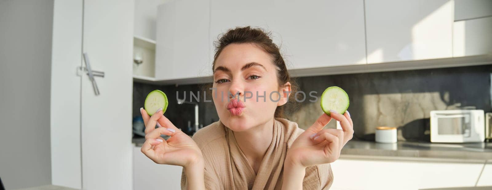 Portrait of beautiful brunette girl cooking in the kitchen, posing in bathrobe at home, holding zucchini, showing happy smile, making healthy food, vegetarian meal.