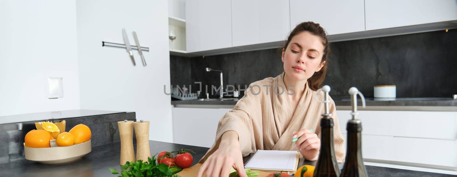 Portrait of woman sitting with groceries, making list for shopping, posing near vegetables, preparing food, cooking in the kitchen by Benzoix