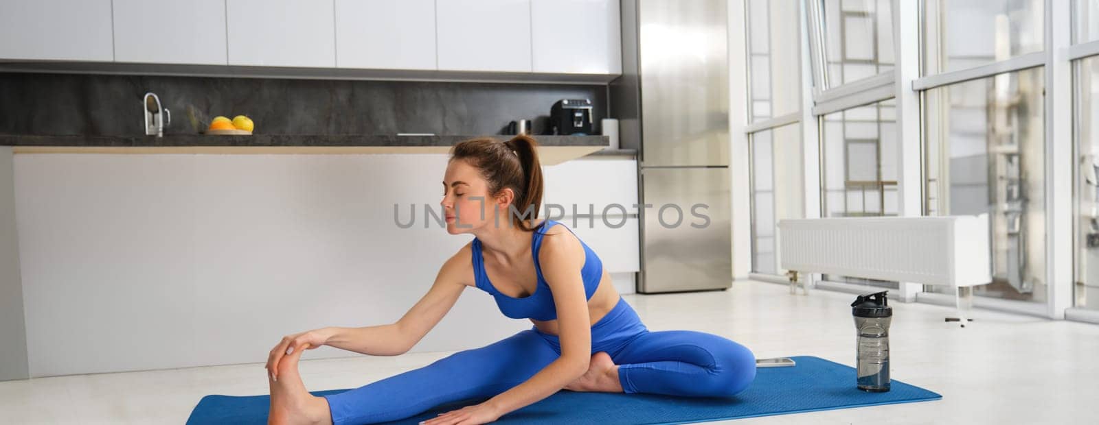 Fitness and workout concept. Young woman stretching her legs, doing exercises at home on yoga mat, doing splits on floor in living room.