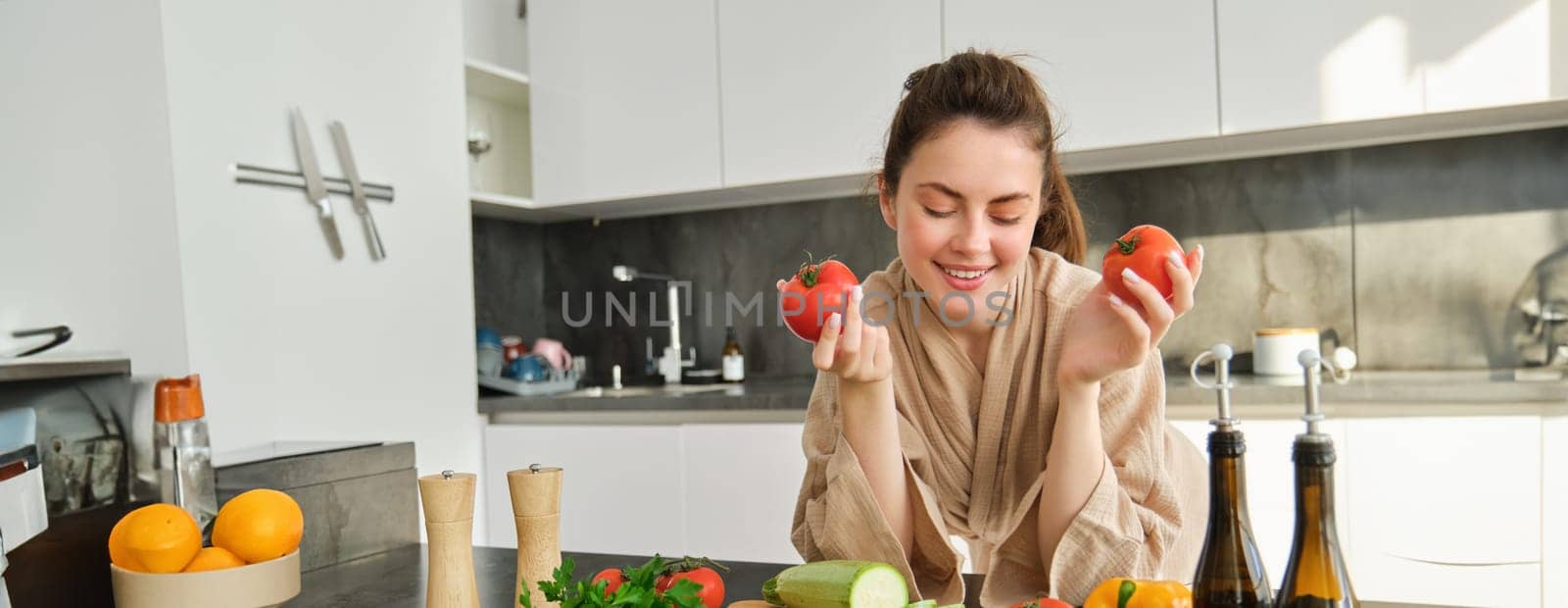 Portrait of beautiful woman cooking in the kitchen, chopping vegetables on board, holding tomatoes, lead healthy lifestyle with preparing fresh salads, vegan meals.