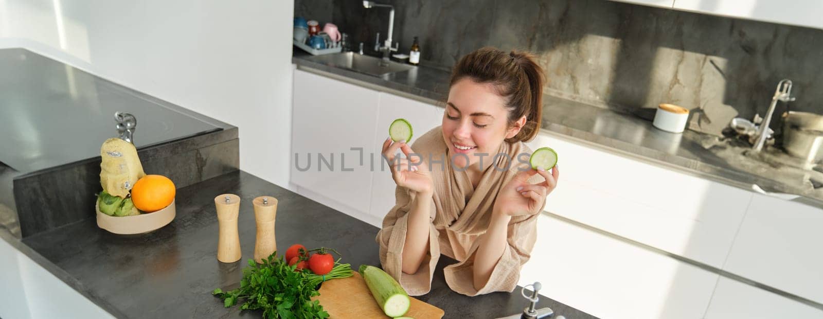 Portrait of beautiful brunette woman in the kitchen, wearing bathrobe, chopping vegetables on board, cooking healthy vegetarian food, preparing salad, making a meal.