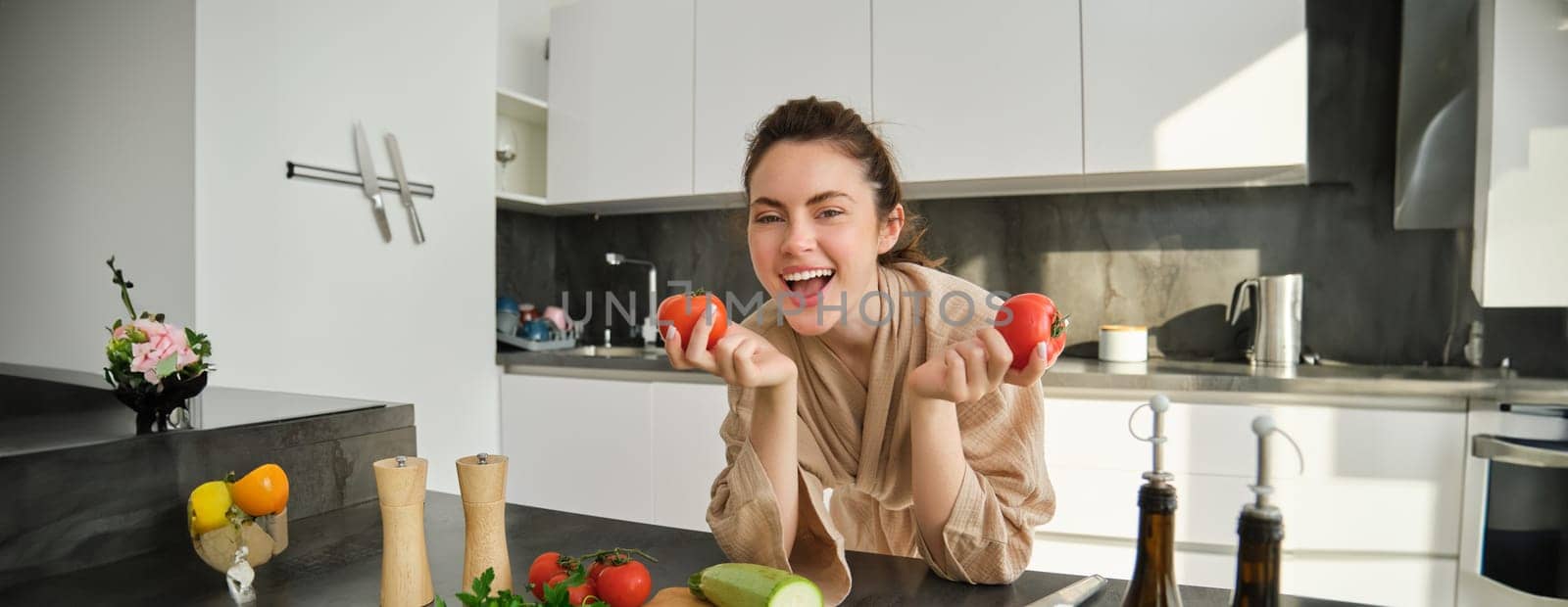 Portrait of beautiful woman cooking in the kitchen, chopping vegetables on board, holding tomatoes, lead healthy lifestyle with preparing fresh salads, vegan meals by Benzoix