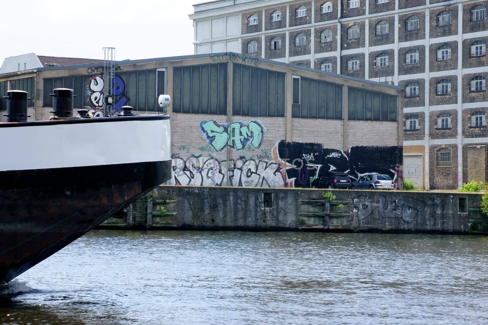 A photograph of a ship's tail passing a warehouse painted with graffiti.