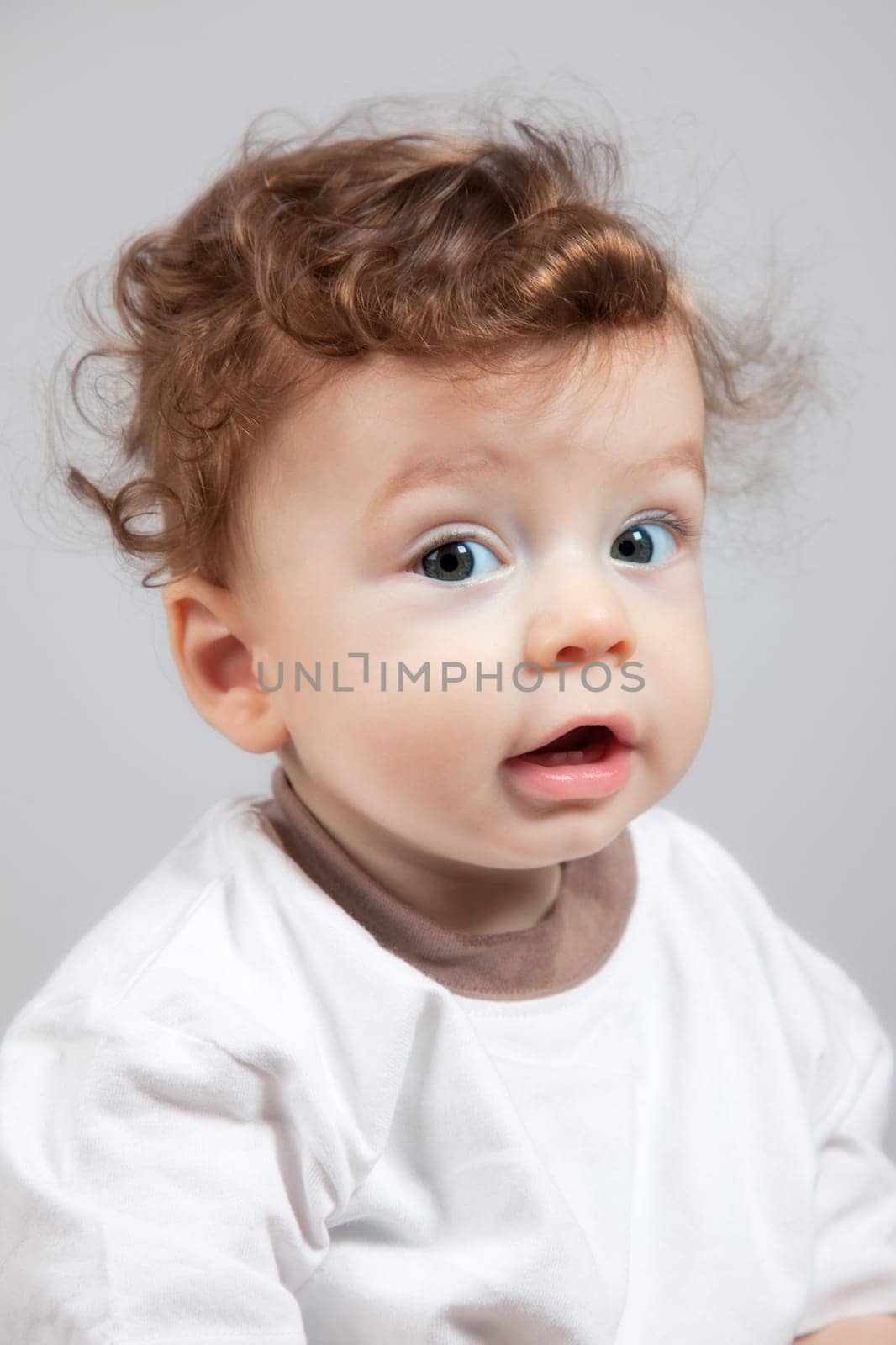 Studio portrait of a happy 8 months old baby boy with curly hair.