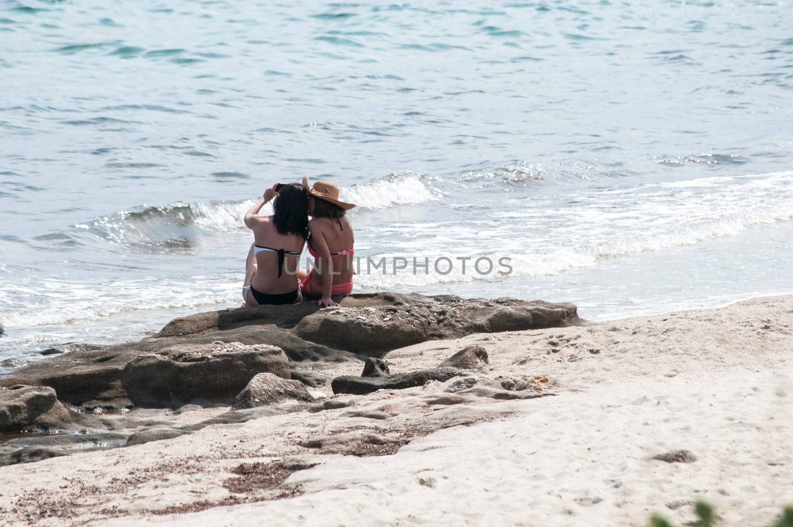Two girls sitting back on sea beach rock
